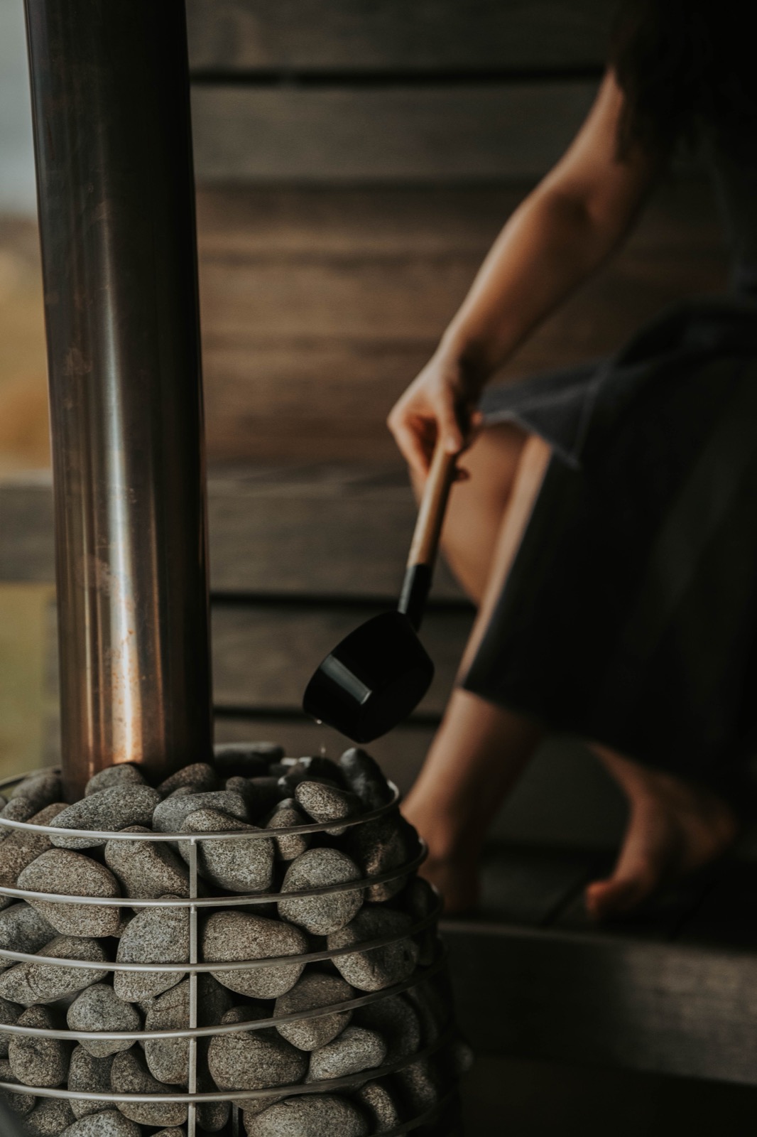 A dimly lit sauna with a stone heater and someone ladling water over the stones